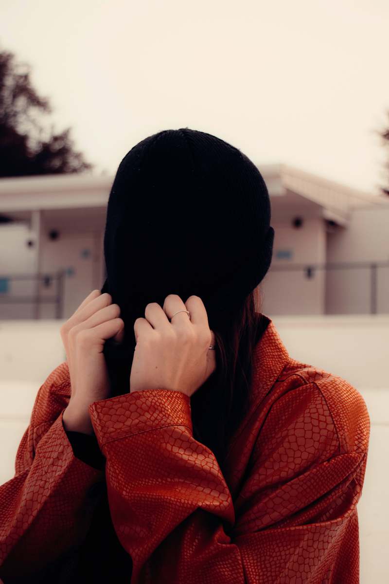 portrait photography woman in red knit sweater covering face with black knit cap beanie